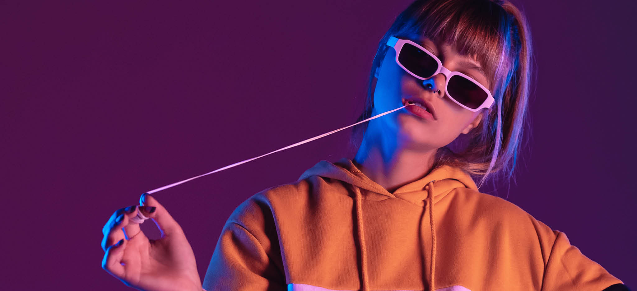 Daring pretty young 20s fashion teen girl model wear glasses chewing bubble gum look at camera stand at purple studio background, igen teenager with bubblegum in trendy night 80s party light portrait