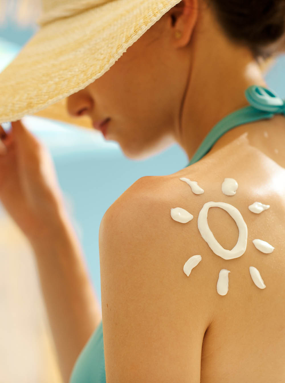 Young beautiful woman tanning at the beach with sunscreen cream on her shoulder, UV protection and skincare concept
