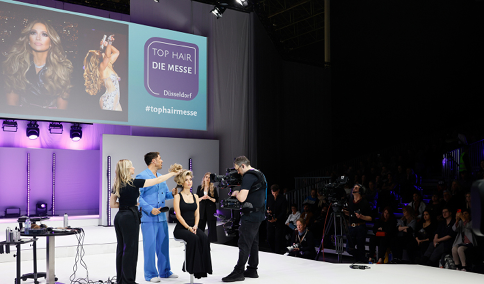 Das Foto zeigt eine Impression der Show New Flag pr sentiert Chris Appleton x Color Wow. Mit Glamour, Charme und tollen Styles: Nicht nur J.Lo und Kim Kardashian werden von Chris Appleton verzaubert. Auf der TOP HAIR Messe 2022 holte er spontan drei Friseurinnen zu sich auf die B hne, um seine Arbeit aus der N he zu betrachten. TOP HAIR - DIE MESSE D sseldorf ist die Leitmesse f r die deutsche Friseurbranche. Hier erfahren die Fachbesucher, was Friseure, ihre Kunden und K pfe jetzt und k nftig bewegt: Trends, Technik, Equipment, Know-How und Salon-Business. Alles, was der Salon zum Erfolg braucht, lernen Friseure in Shows, Workshops, Kongress-Vortr gen, der Barber's Experience und der Fachausstellung kennen. Mit ber 400 Ausstellern und Marken und  ber 1.000 B hnen-Akteuren wird die TOP HAIR D sseldorf j hrlich zwei Tage lang zum Kreativ-Hot-Spot und Wissens-Pool f r Friseure - beste Unterhaltung und Vernetzung inklusive.    