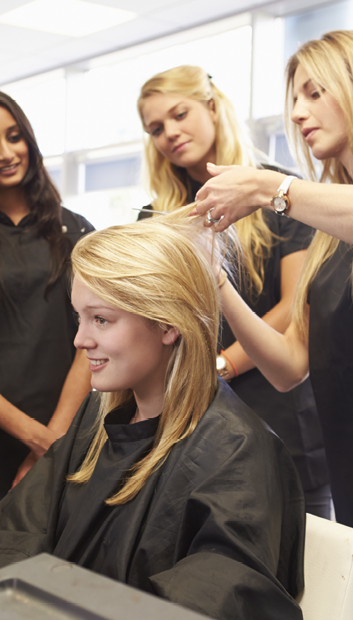 Teacher Helping Students Training To Become Hairdressers