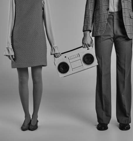 cropped view of couple in colorful clothes standing with yellow boombox on grey, vintage lifestyle