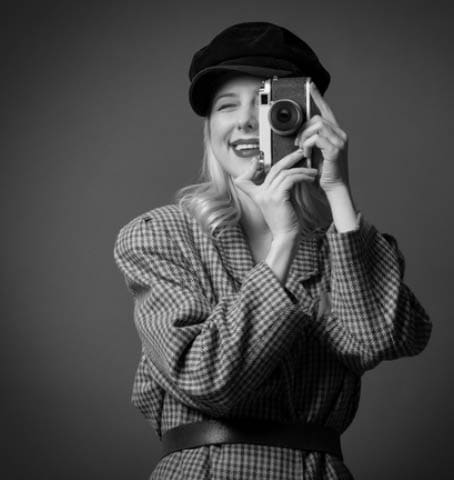 woman in British style jacket and beret with vintage camera on green background