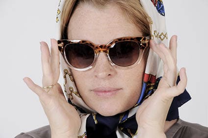Young woman is wearing scarf and sunglasses in a Grace Kelly Style. Studio shot with light background. Isolated.