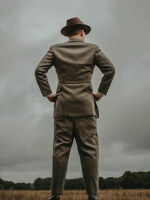 30 year old man entire body and legs back view looking toward horizon dressed in 1940s suit with fedora hat hands on hips