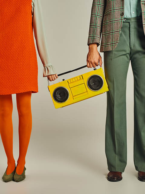 cropped view of couple in colorful clothes standing with yellow boombox on grey, vintage lifestyle